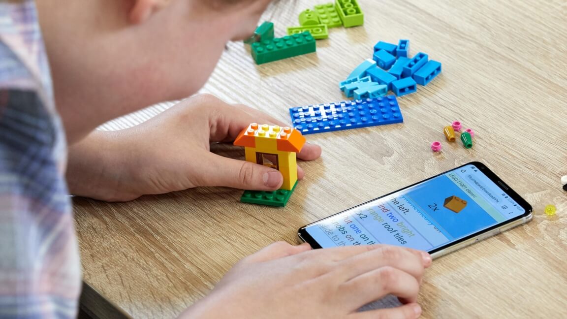 Nærbillede af Thea, der bygger med LEGO. Der ligger en mobil med instruktioner ved siden af hende. 