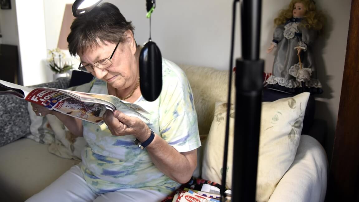 Grethe sidder og læser Familie Journal med bladet helt tæt på og skarpt lys tændt 
