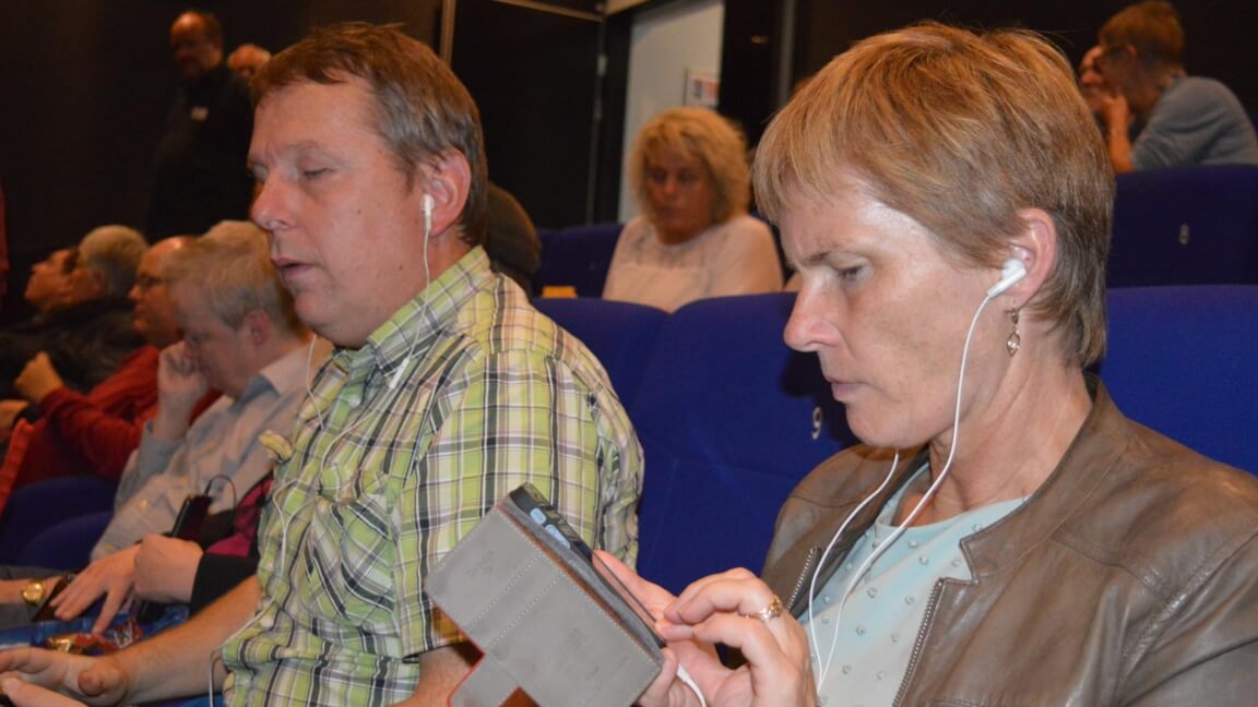 En mand og kvinde ser film i Jelling Biograf. De har begge høretelefoner på. 