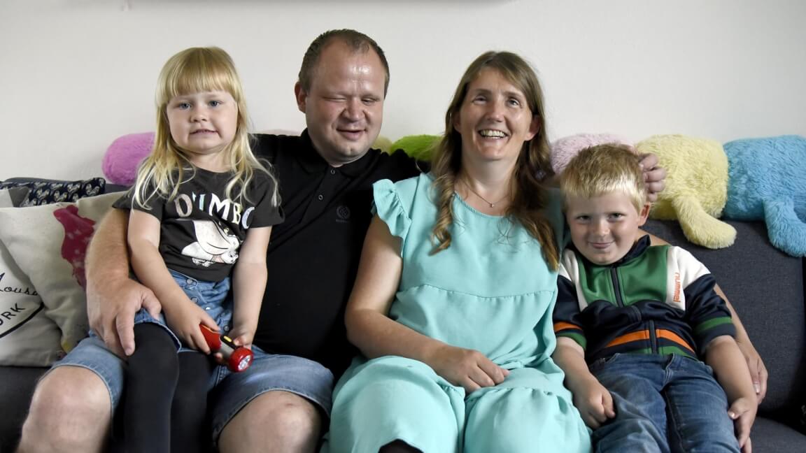 Hele familien sidder i sofaen og smiler med Brian og Tanja i midten og et barn på hver side