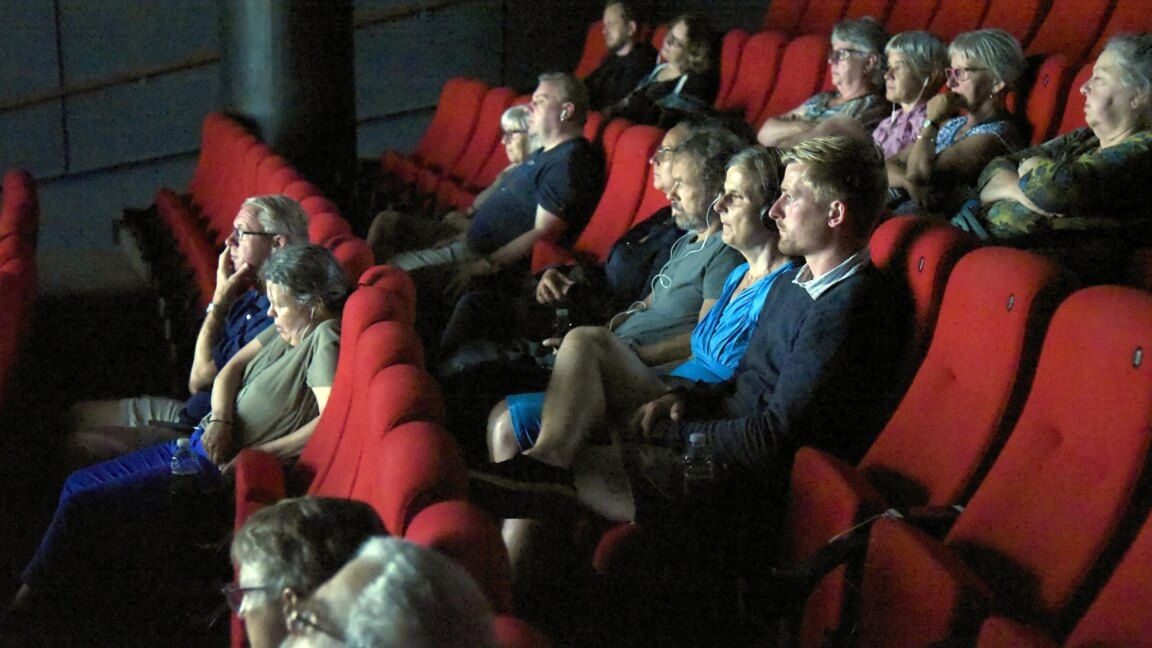 Folk sidder i røde biografsæder med høretelefoner 