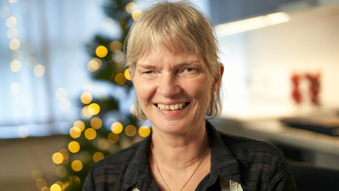 Portræt af Anette Bjerre iført forklæde. I baggrunden står et juletræ med lys