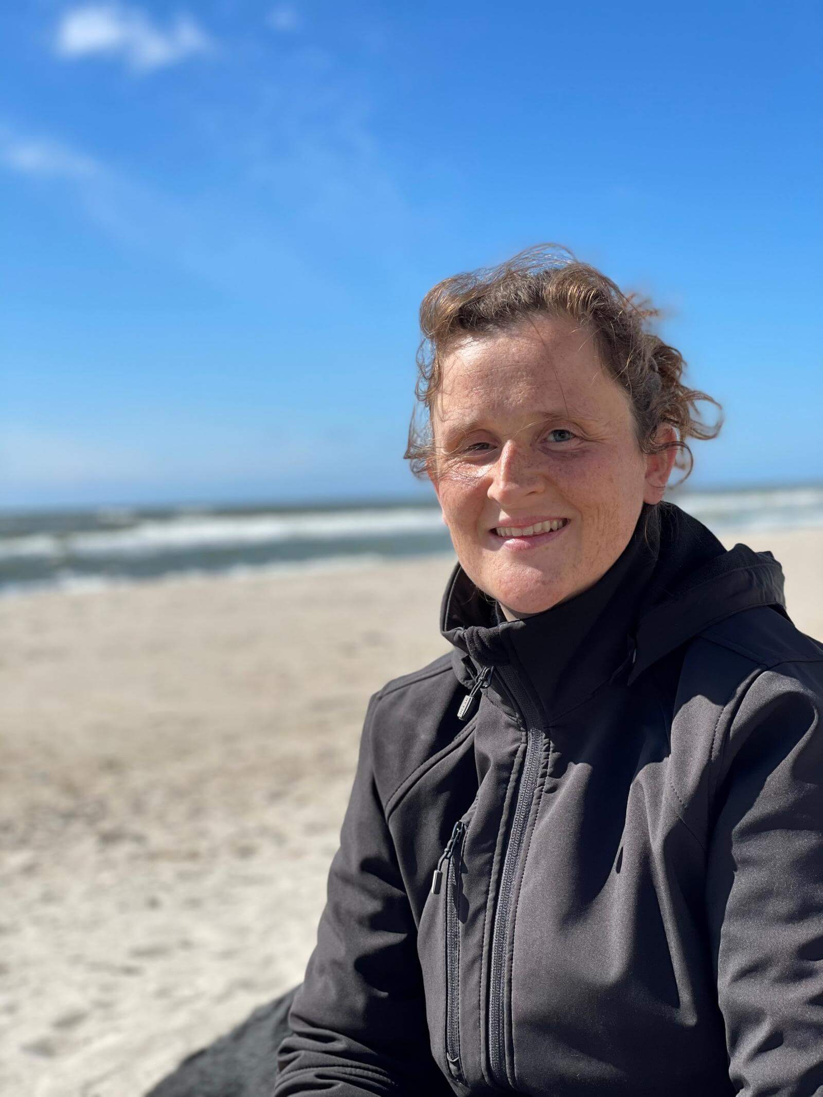 Portræt af Ann-Sofie på en strand med blå himmel og havet i baggrunden