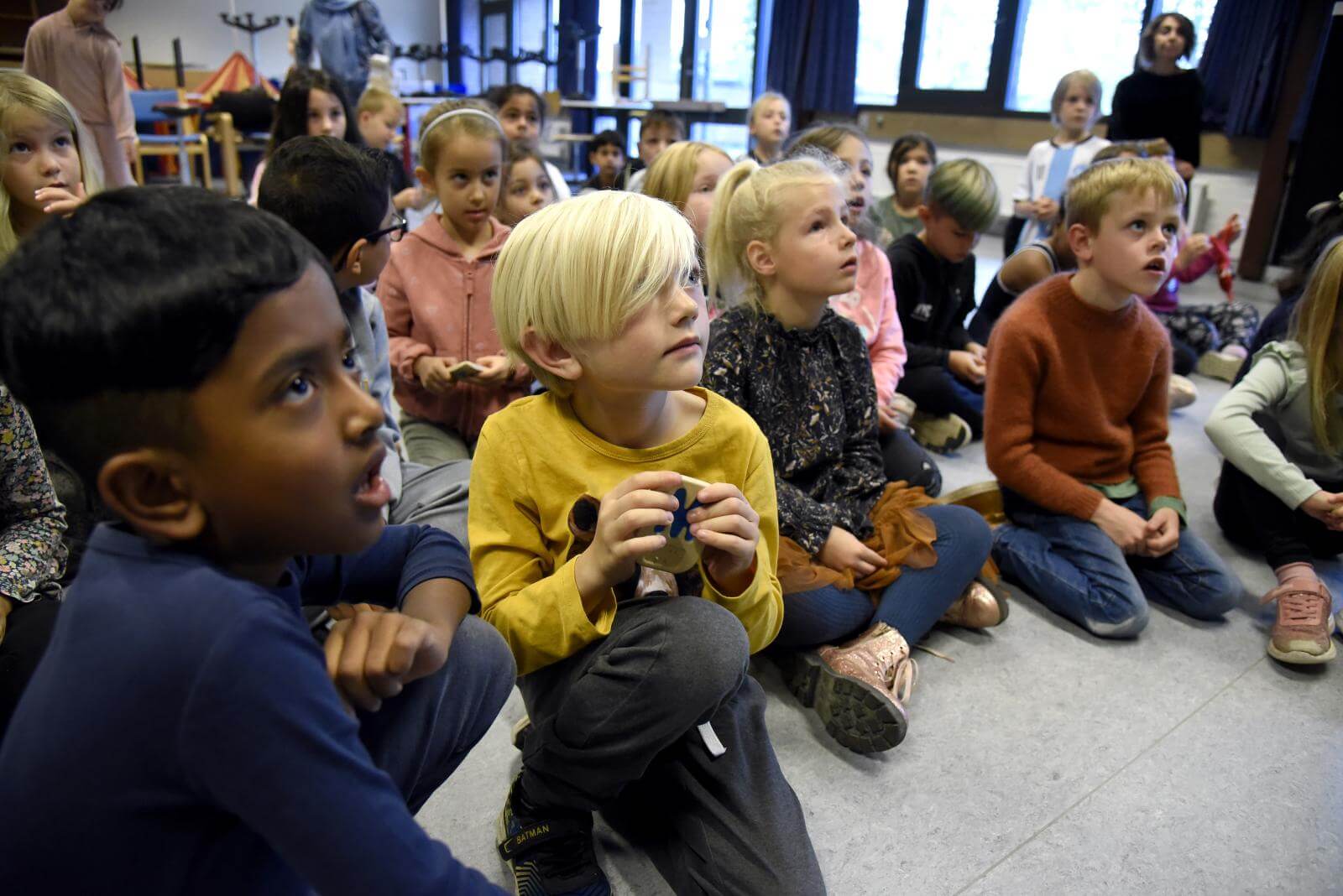 Nærbillede af skoleelever der sidder på gulvet og kigger opmærksomt på Ask