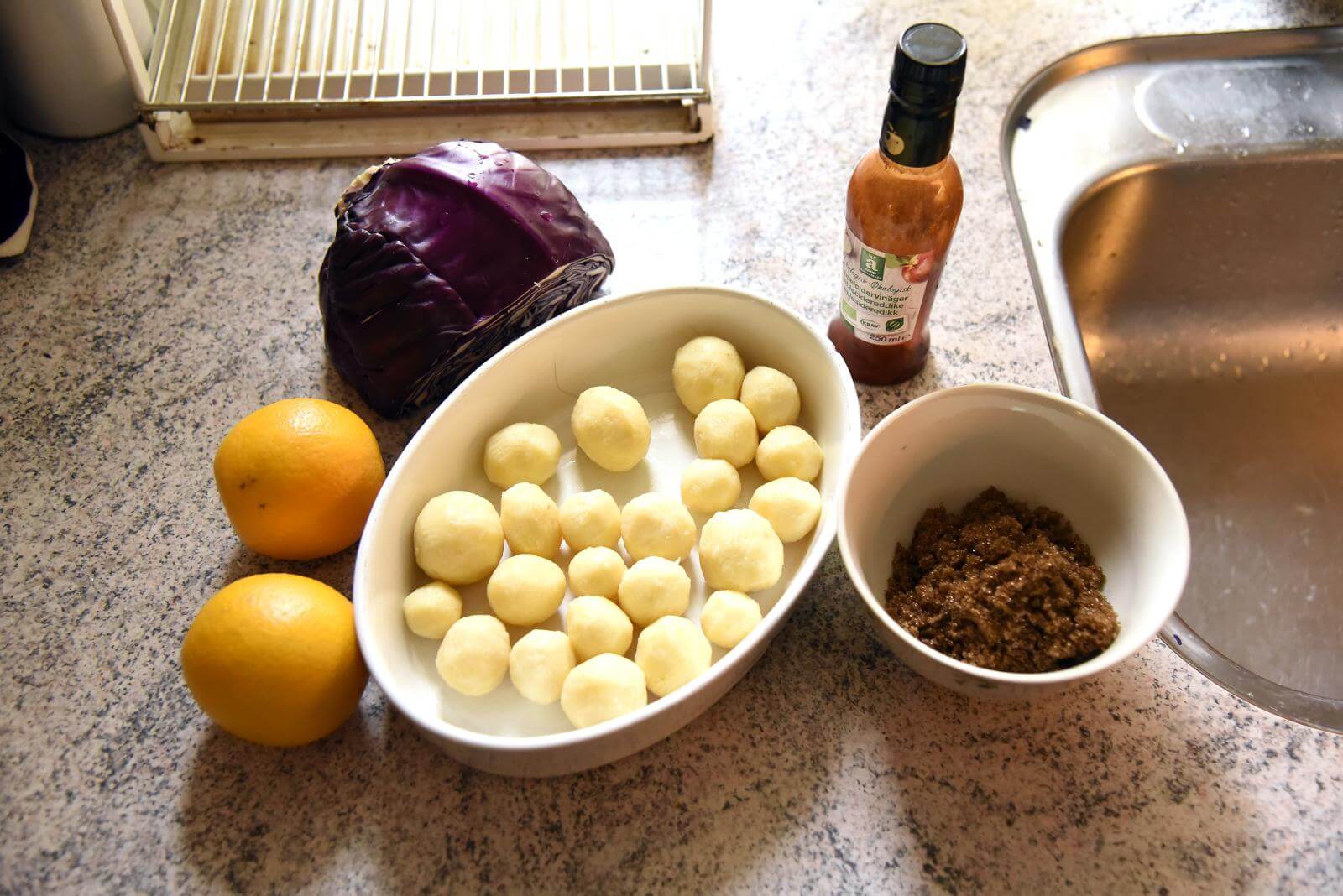 Ingredienser er funder frem på køkkenbordet. Appelsiner, rødkål, kartofler og brun farin