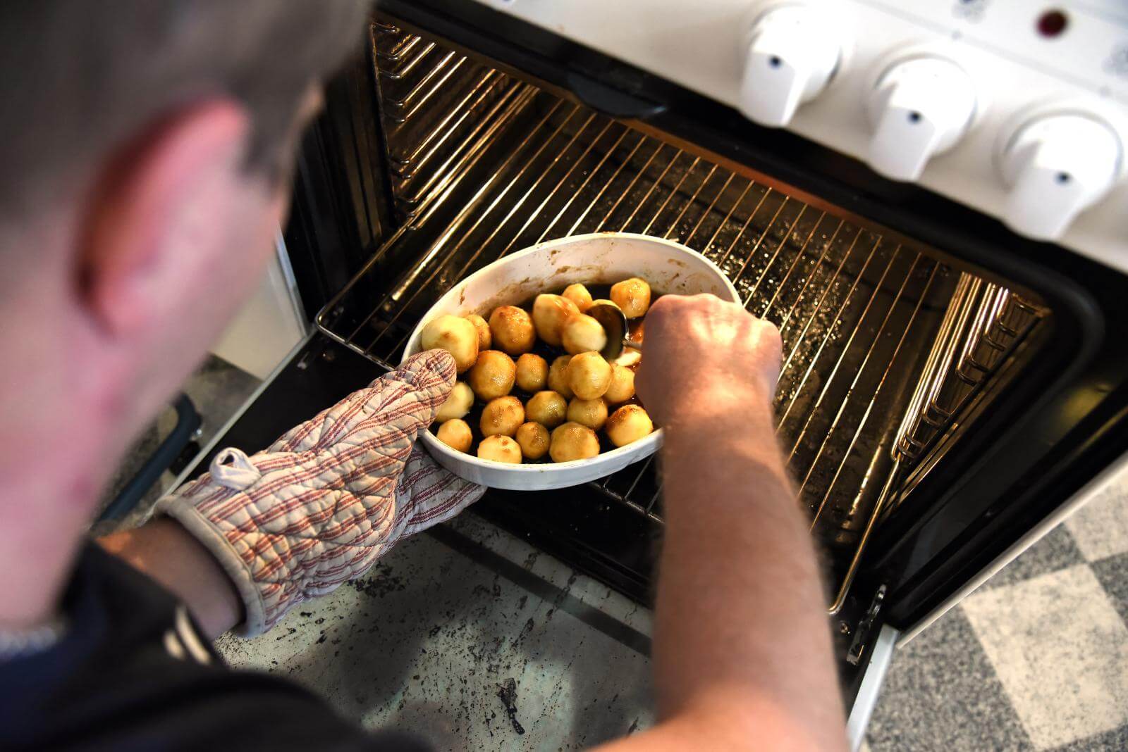 Lasse holder fadet med brunede kartofler i den ene hånd med grillhandske, mens han stikker i kartoflerne med den anden hånd for at undersøge, om de er færdige
