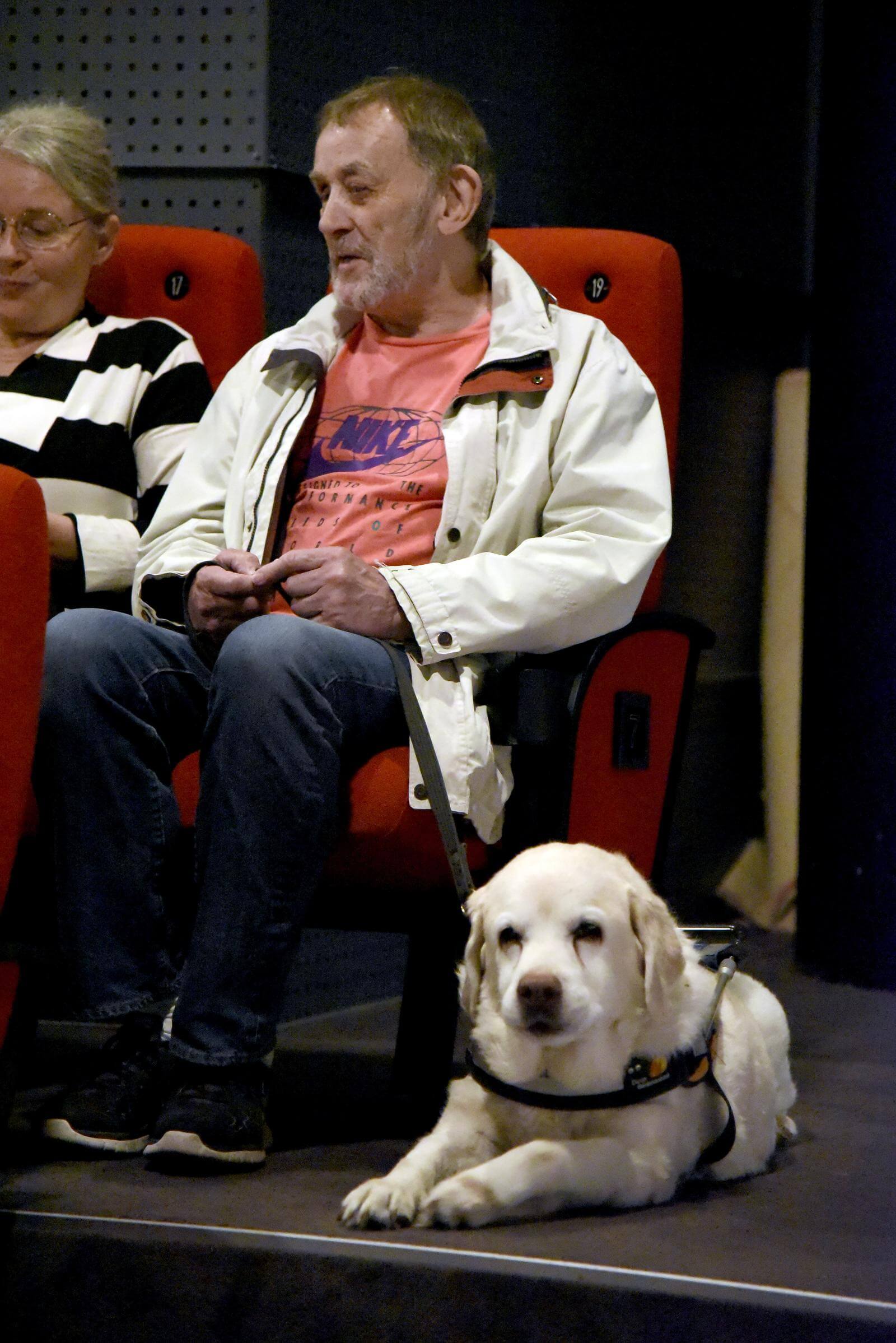 Portræt af Ole og hans ledsager, der sidder i biografstole. Ved siden af ligger Oles førerhund 