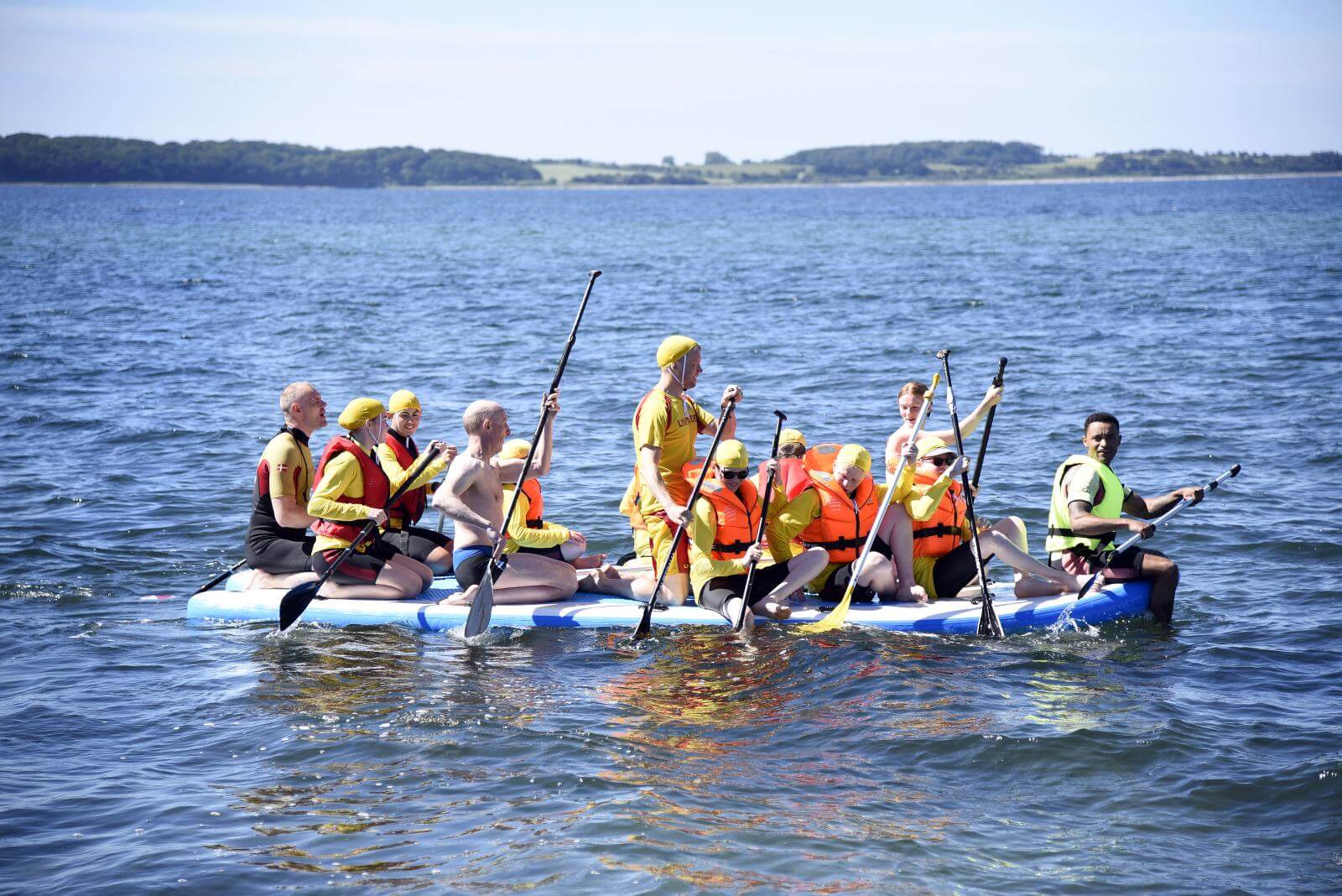 Et hold af 12 ældre elever roer på en stor oppustelig gummibåd i fjorden med to livreddere. Alle iført våddragter, redningsveste og gule badehætter
