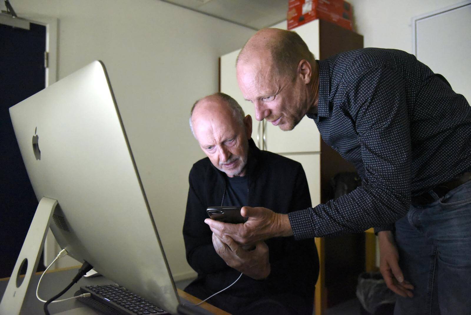 Henning sidder foran sin skærm og er ved at undersøge noget på mobilen, som han får hjælp til af underviseren