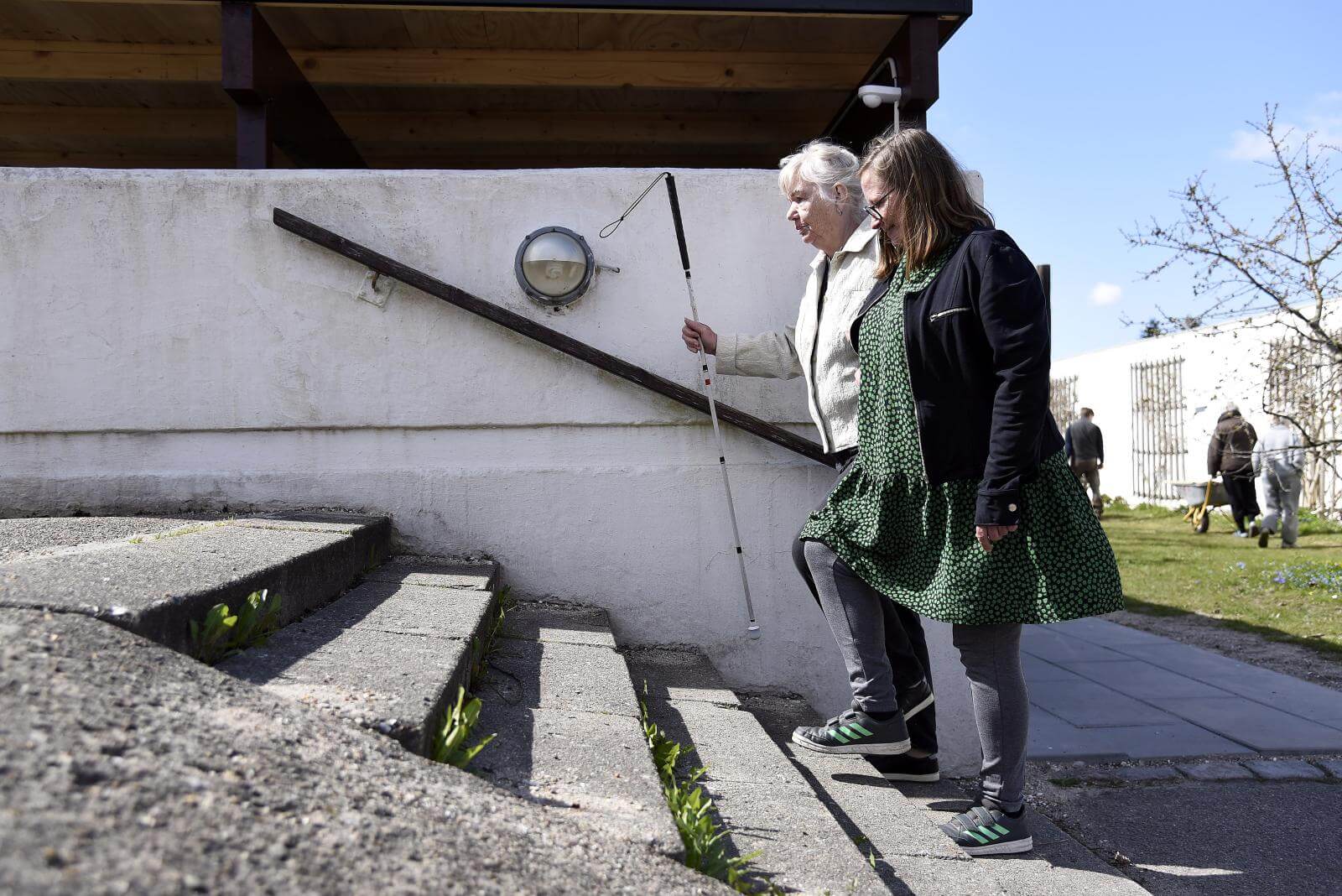 Tove får en støttende arm ad sin ledsager Maria, mens de går op ad trapper