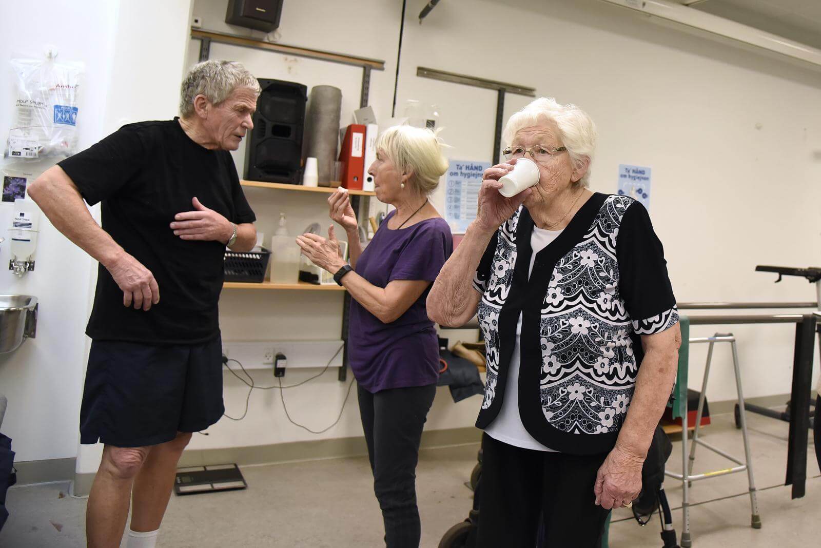 88-årige Gurli drikker vand, mens hendes to holdkammerater snakker i baggrunden