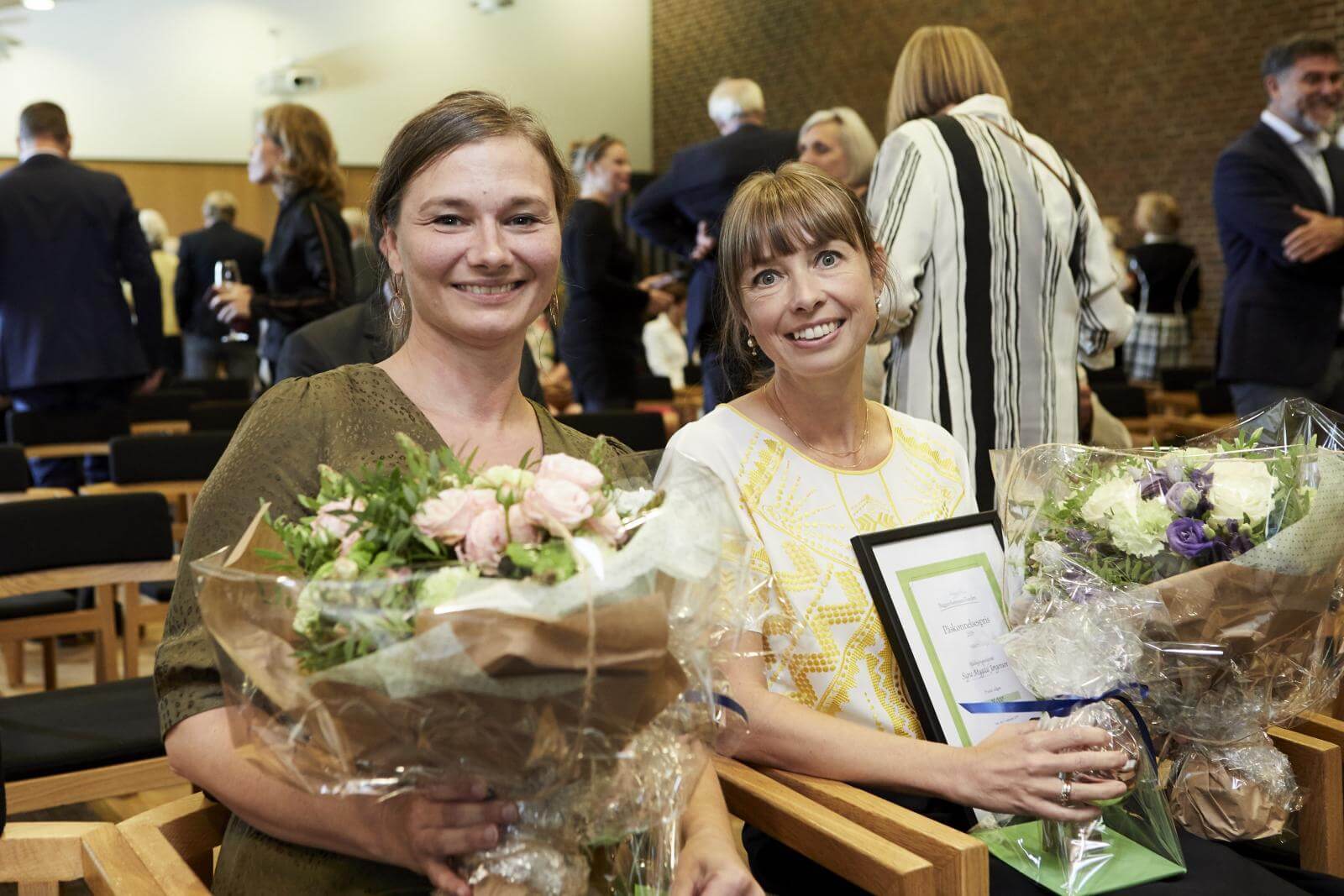 To glade øjensygeplejersker med diplom og blomster i hånden