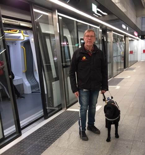 Preben står med førerhund og blindestok foran Københavns metro