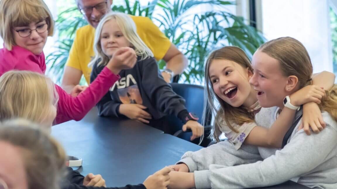 En gruppe børn sidder omkring et bord og hygger sig og griner.