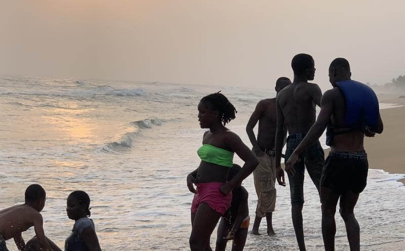 Silhuetter af børn som leger i havet på stranden, mens solen er ved at gå ned