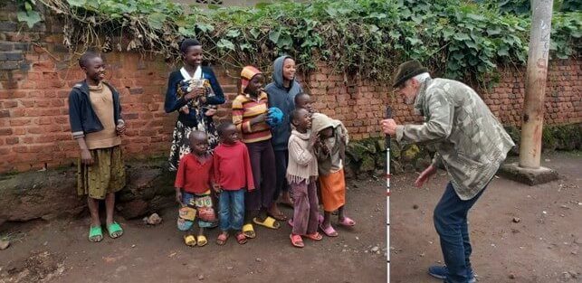 Jens Hviid står med sin hvide stok foran en flok rwandiske børn, som griner og smiler til ham.