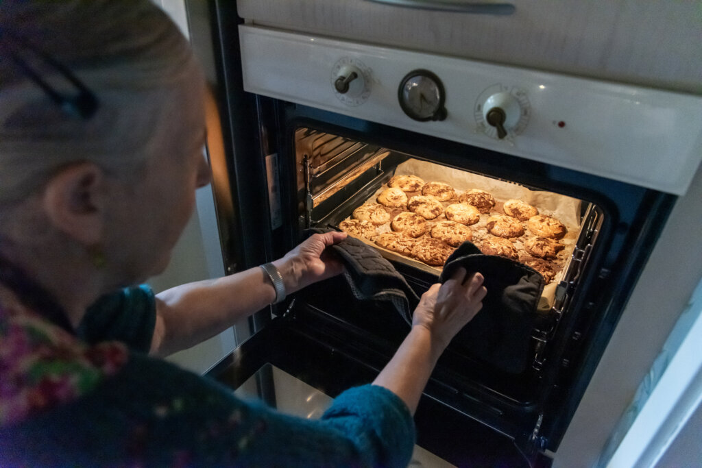 Mette er udstyret med grydelapper og tager en bageplade med småkager ud af ovnen