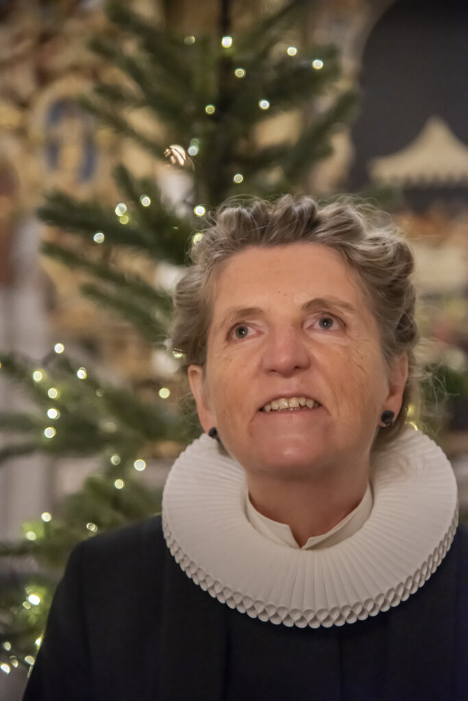 Portræt af Rita iført præstekjole. I baggrunden ses et juletræ med tændte julelys