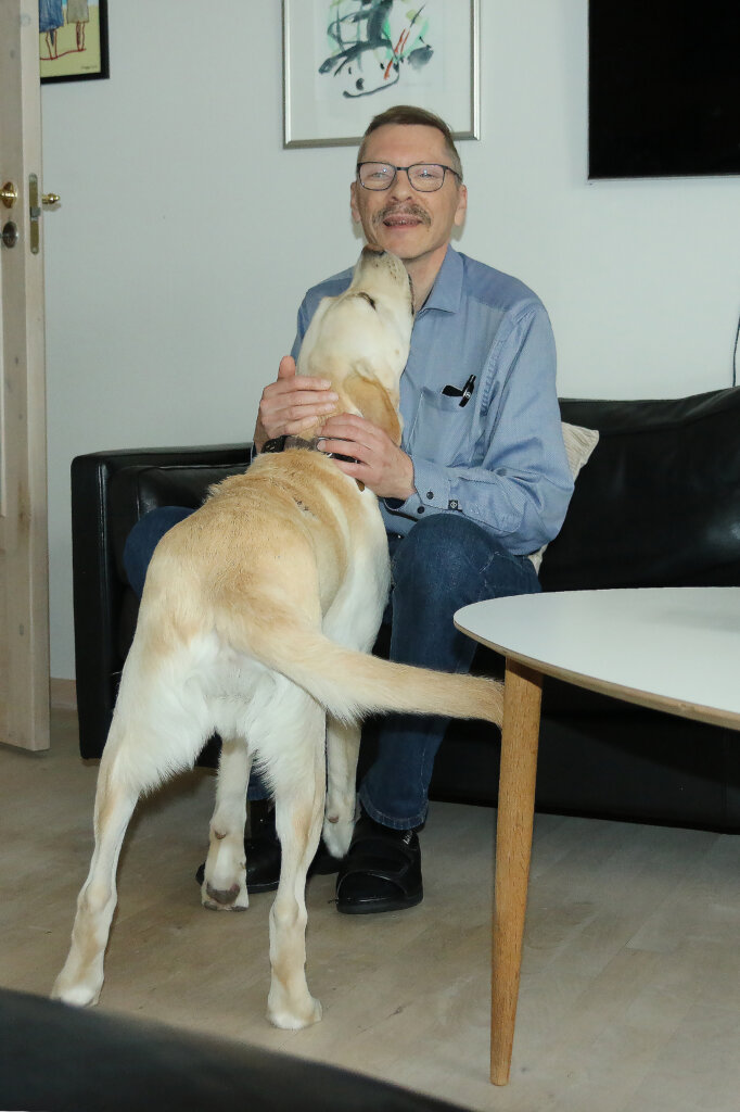 Førerhunden Milo, en lys labrador, slikker Johan på hagen, som sidder i sin sofa