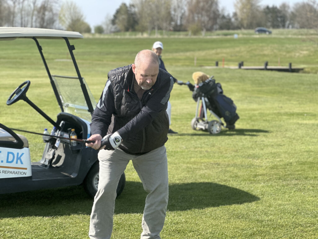 Flemming gør klar til at skyde til golfbolden. I baggrunden holder en golfbil