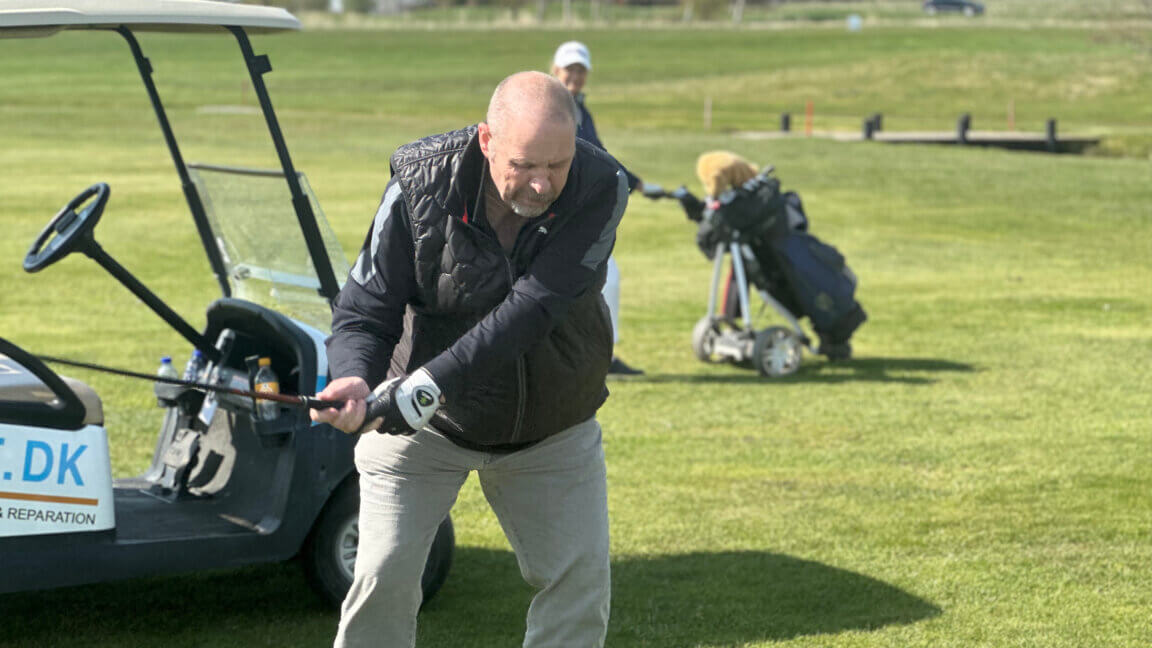 Flemming gør klar til at skyde til golfbolden. I baggrunden holder en golfbil