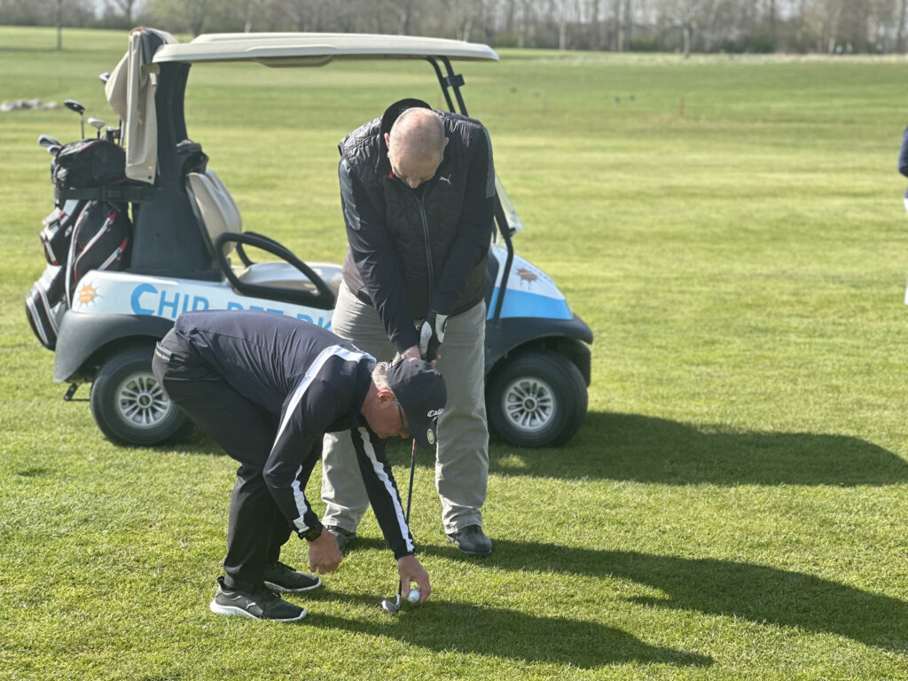 Finn placerer bolden foran Flemming golfkølle, der er klar til at skyde