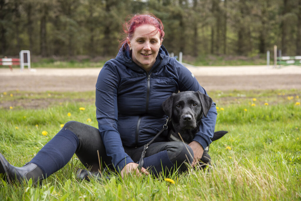 Rikke sidder i græsset og holder en arm om førerhunden Silke, en sort labrador