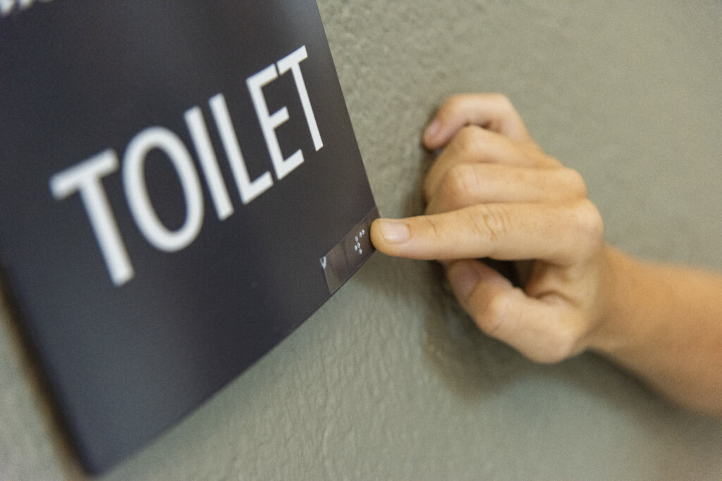 Billede af Sofies hånd, som læser, at der står "toilet" skrevet  med punktskrift 