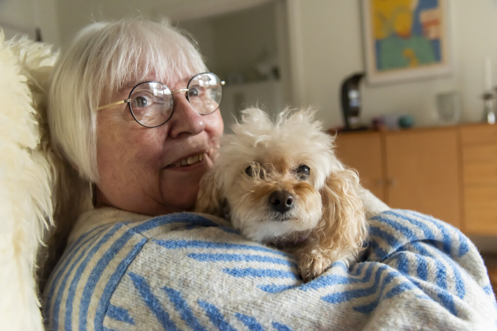 Birthe sidder i sin lænestol og holder tæt om hendes lille pjuskede hund