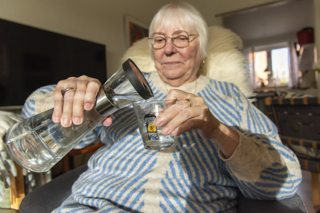 Birthe hælder vand i sit vandglas ved at stikke fingereb i glasset