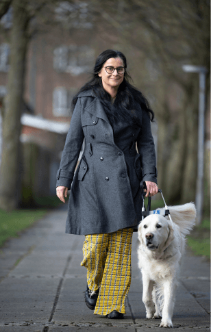 Tijana går på fortovet med førerhunden Buster, en lys golden retriever iført førerhundebøjle