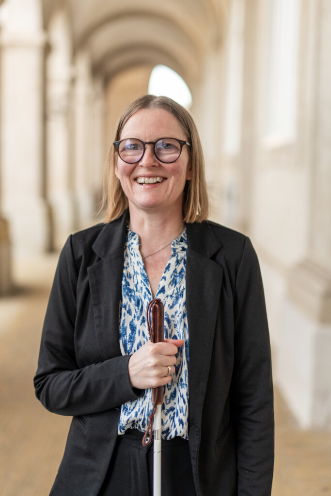 Diana står smilende uden for med sin blindestok i en buegang
