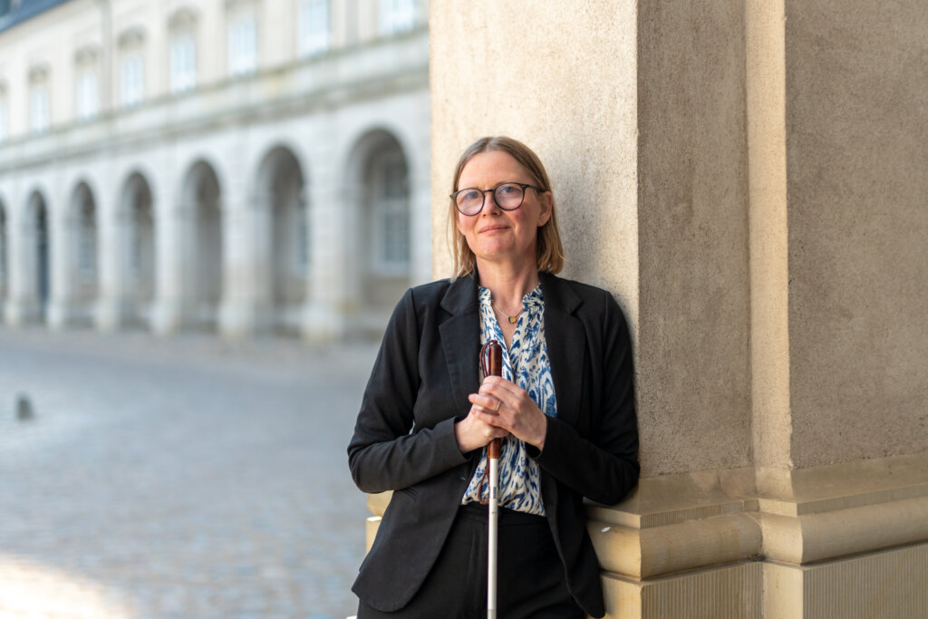 Diana Stentoft står uden for med sin blindestok og læner sig op ad en søjle