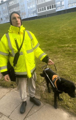 Søren går på fortovet med Pelle i førerhundebøjle, en sort labrador.