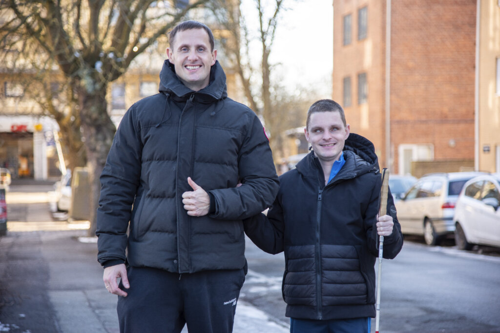 Portræt af Benjamin Hav og Nicklas udenfor. Benjamin giver en arm til Nicklas, der står med sin blindestok i den anden hånd. De smiler begge