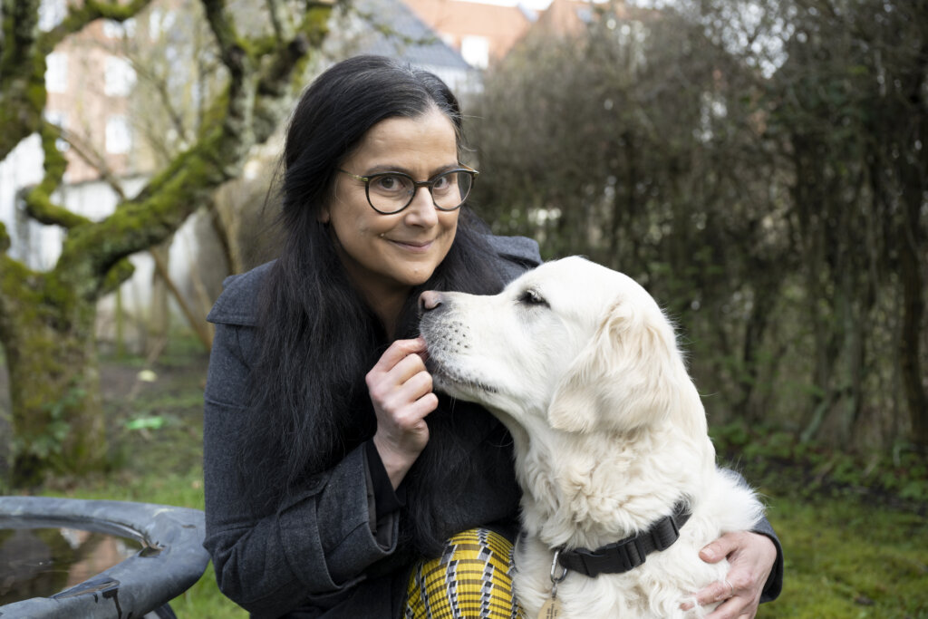 Tijana sidder på hug uden for og giver førerhunden Buster en godbid, en lys golden retriever