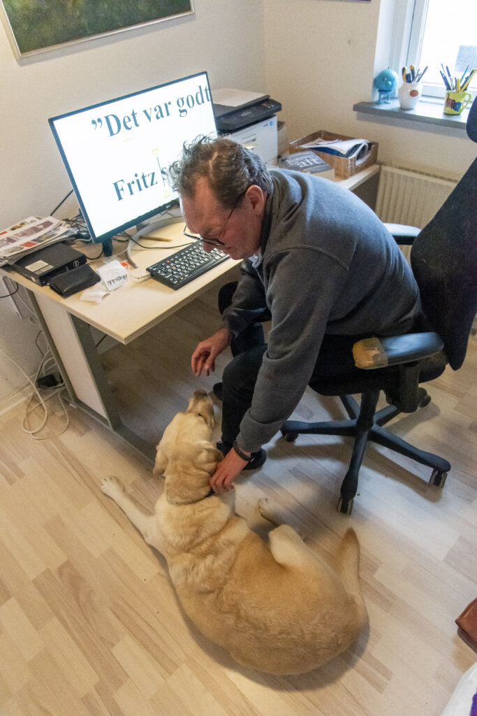 Finn sidder ved et skrivebord med computer, mens Baloo ligger ved siden af og bliver klappet