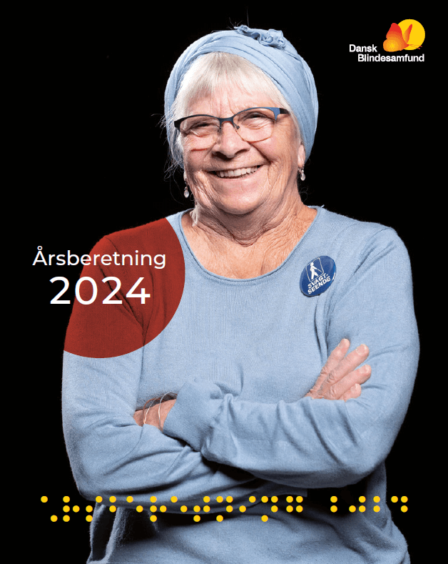 Forsiden af Årsberetningen 2024. En ældre kvinde står med armene over kors i en blå bluse og smiler til kameraet. Hun har briller og et badge med manden med den hvide stok på. I en rød cirkel står der: Årsberetning 2024. I bunden står der med gul punktskrift Årsberetning 2024.