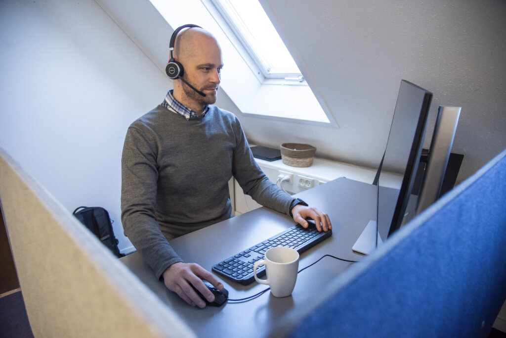Kristoffer sidder ved sin computer p&aring; kontoret med h&oslash;retelefoner med mikrofon p&aring;
