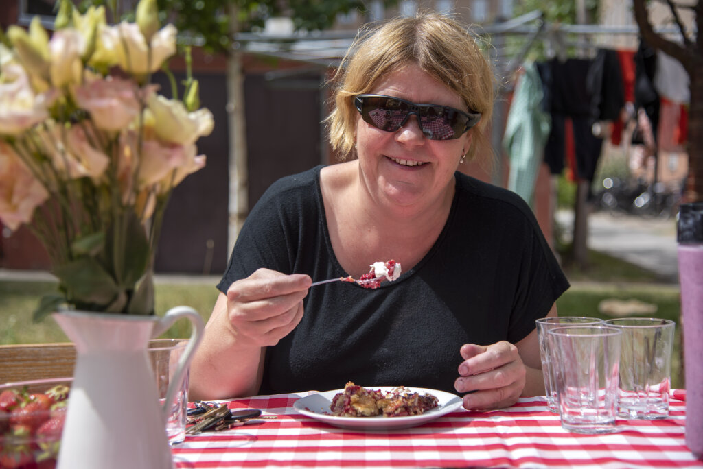 Lene spiser hindb&aelig;rt&aelig;rte p&aring; en b&aelig;nk uden for med r&oslash;dternet dug