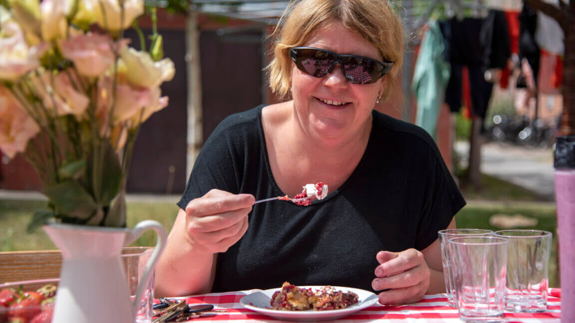 Lene spiser hindbærtærte på en bænk uden for med rødternet dug