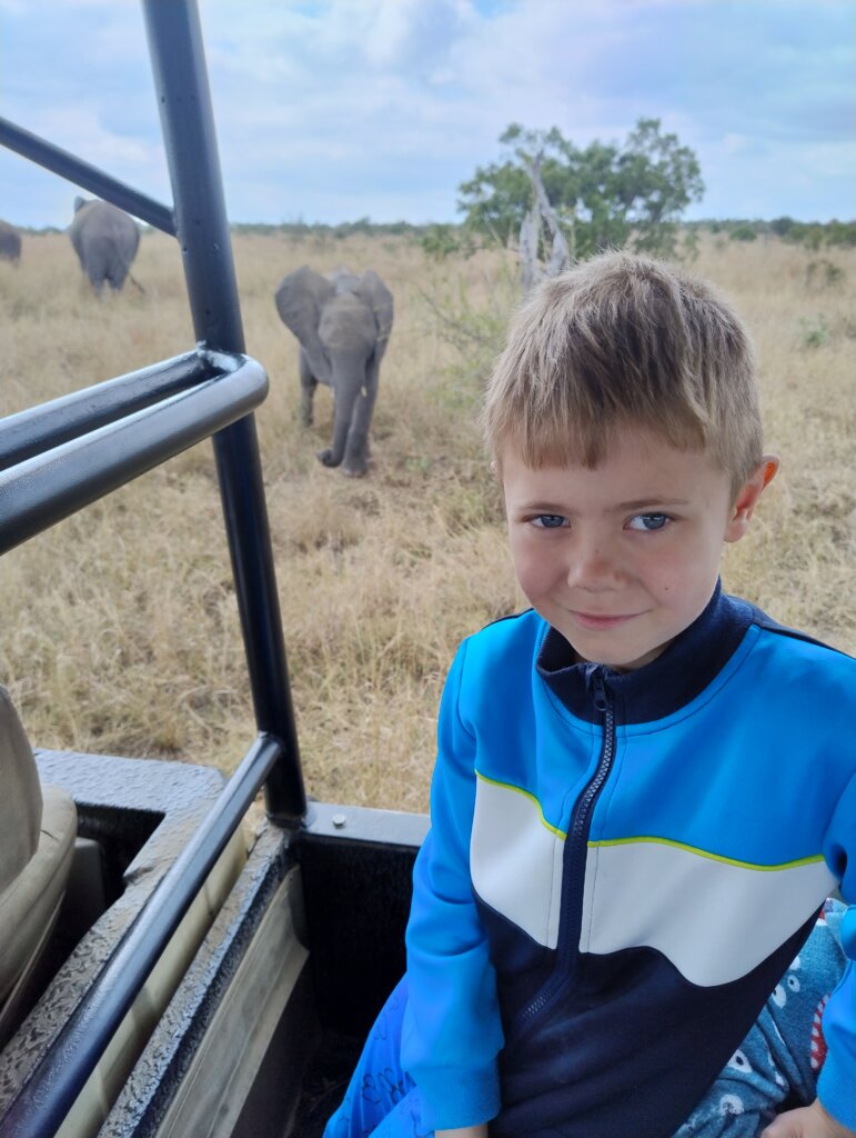 Marco sidder i en jeep p&aring; safari. I baggrunden ses elefanter