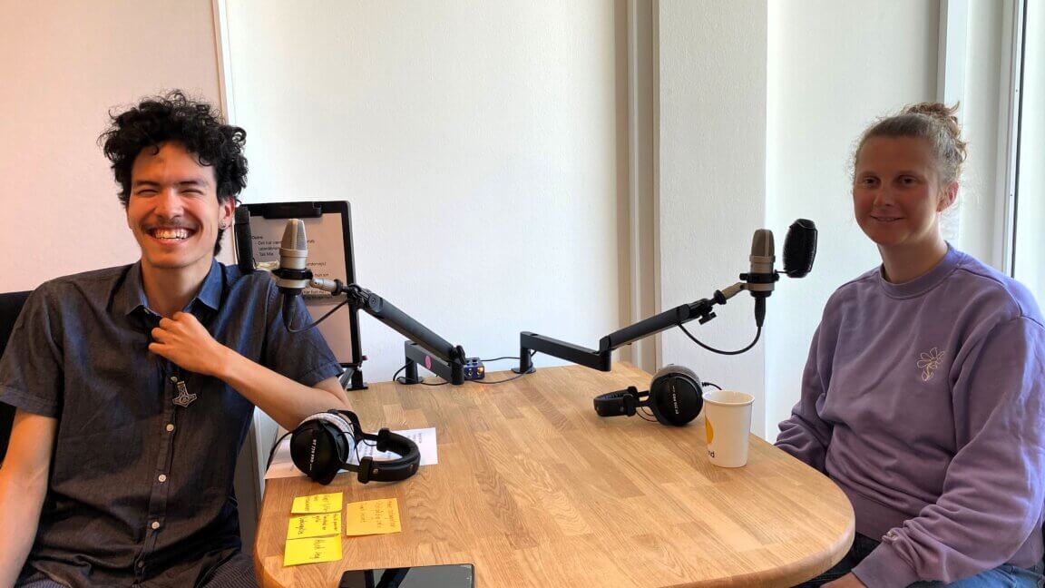 Podcastvært Tor sidder over for Mie Prip Henriksen ved et bord, hvor der står to mikrofoner