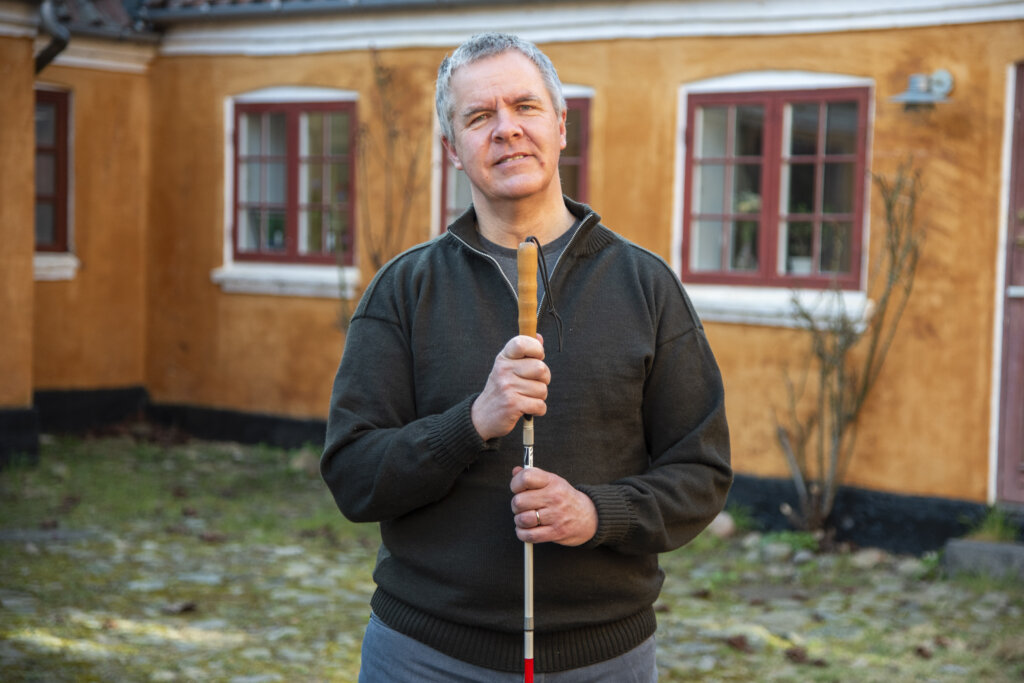 Portr&aelig;t af Mikael som st&aring;r uden for sit hjem med begge h&aelig;nder p&aring; blindestokken