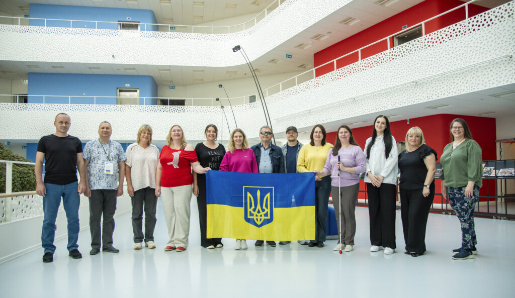 Gruppebillede af medlemmer fra forskellige ukrainske blindeorganisationer. De holder et stort ukrainsk flag