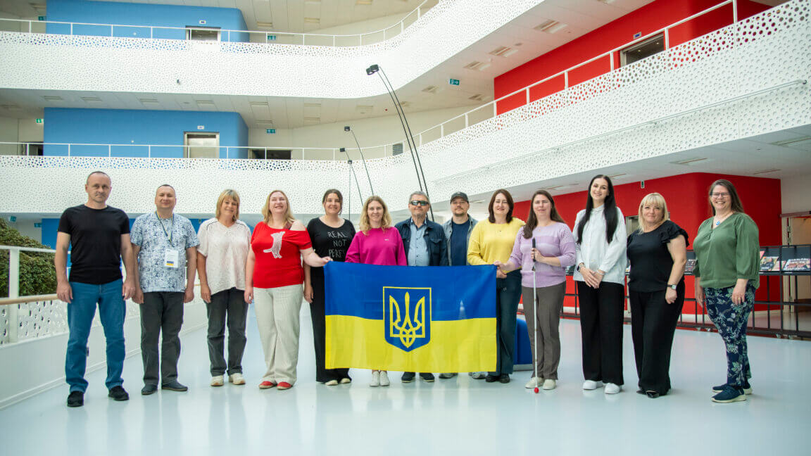 Gruppebillede af medlemmer fra forskellige ukrainske blindeorganisationer. De holder et stort ukrainsk flag