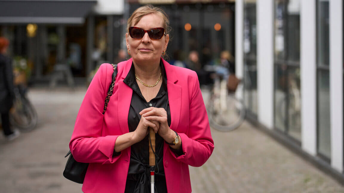 Portræt af Anette som står i en gågade med begge hænder på blindestokken