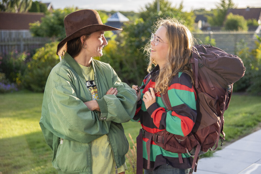 Amalie og Mille griner til hinanden. Mille st&aring;r med en cowboyhat og Amalie har backpacker taske p&aring; ryggen.