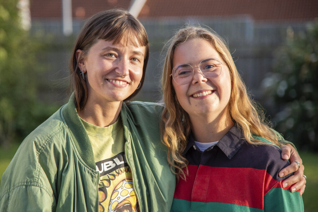 Mille og Amalie holder om hinanden og smiler. De st&aring;r uden for