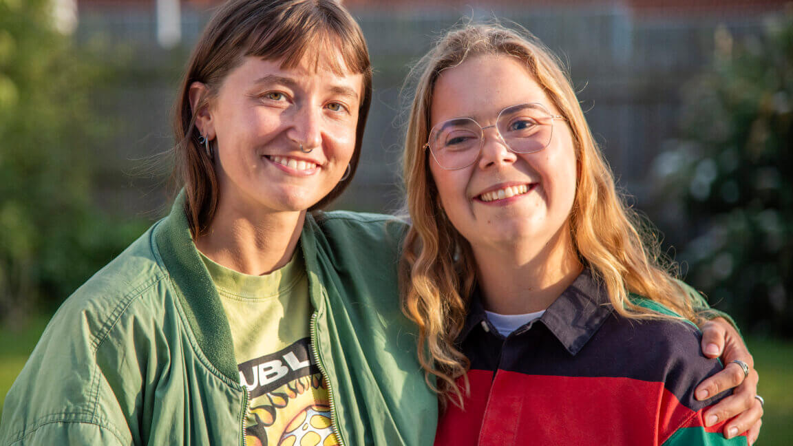 Mille og Amalie holder om hinanden og smiler. De står uden for